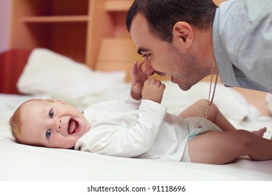 Young Happy Father Playing  With Baby Lying In Bed. Baby Want To Catch Father's Face