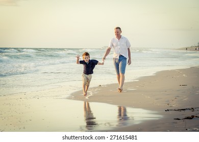 Young Happy Father Playing On The Beach With Little Son Running Excited With Barefoot In Sand And Water, The Kid Smiling And Having Fun Together With Dad In Summer Vacation Concept 