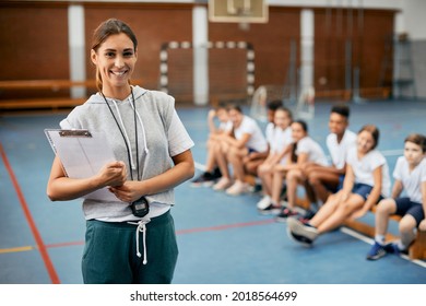 Young happy female coach looking at camera while having PE class with elementary students at school gym.  - Powered by Shutterstock