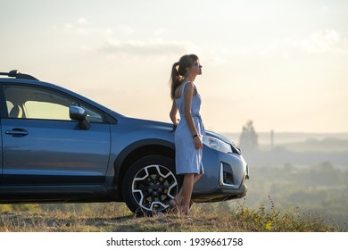 Junge glückliche Autofahrerin, die sich in der Nähe ihres Autos ausruht und bei Sonnenuntergang die Natur im Sommer bewundert. Reiseziele und Freizeitkonzept.