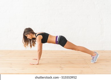 Young happy female sportswoman making push-ups on background white brick wall