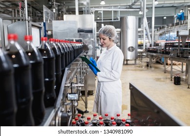 Young happy female worker in bottling factory checking juice bottles before shipment. Inspection quality control. 