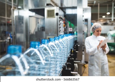 Young happy female worker in factory writing notes about water bottles or gallons before shipment. Inspection quality control. Selective focus.