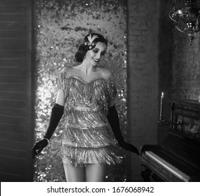 Young happy flapper beautiful woman. finger wave hairstyle headband. short sexy silver dress, smile face. model poses dances. backdrop old classic interior. Black and white photo. Style roar Party 20s