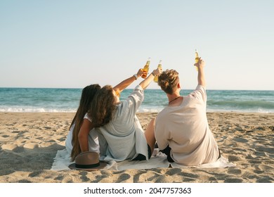 Young happy friends doing picnic and cheers with bottles seaside. Group of people drinking beer together on the beach. - Powered by Shutterstock