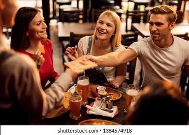 Young Happy Friends Enjoying In Lunch In Tavern And Paying Bill To A Waiter. 