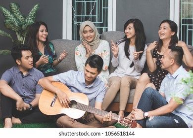Young happy friends having party, one playing guitar and the other singing together - Shutterstock ID 1056518144