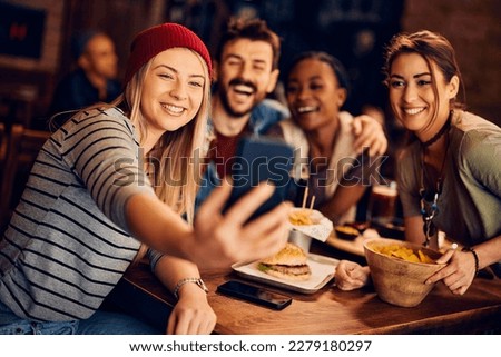 Young happy friends taking selfie with cell phone while  gathering in a bar.
