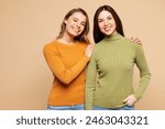 Young happy friends two women they wear orange green shirt casual clothes together hug cuddle put hand on shoulder look camera isolated on plain pastel light beige background studio. Lifestyle concept