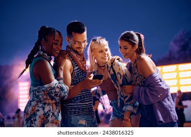 Young happy friends using mobile phone while attending live performance during summer music festival.  - Powered by Shutterstock