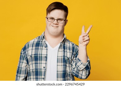 Young happy fun cool smiling man with down syndrome wears glasses casual clothes look camera showing victory sign isolated on pastel plain yellow color background. Genetic disease world day concept