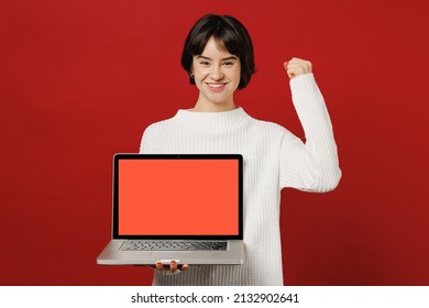 Young happy fun excited woman 20s wearing white knitted sweater holding use work on laptop pc computer with blank screen workspace area do winner gesture isolated on plain red color background studio. - Shutterstock ID 2132902641