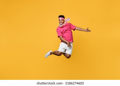 Young happy fun exultant jubilant expressive man 20s he wear pink t-shirt near hotel pool jump high play guitar look camera isolated on plain yellow background studio. Summer vacation sea rest concept