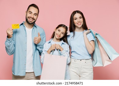 Young Happy Fun Parents Mom Dad With Child Kid Daughter Teen Girl In Blue Clothes Holding Package Bags With Purchases After Shopping Credit Card Show Thumb Up Isolated On Plain Light Pink Background.