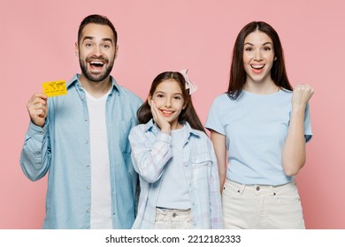 Young Happy Fun Parents Mom Dad With Child Kid Daughter Teen Girl In Blue Clothes Hold In Hand Credit Bank Card Do Winner Gesture Isolated On Plain Pastel Light Pink Background. Family Day Concept.