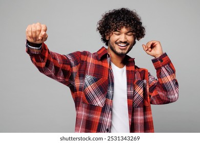 Young happy fun smiling cheerful Indian man he wears red shirt casual clothes dancing celebrate clenching fists close eyes isolated on plain grey color background studio portrait. Lifestyle concept - Powered by Shutterstock