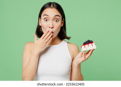 Young happy fun woman wear white clothes holding in hand pice of cake dessert cover mouth isolated on plain pastel light green background. Proper nutrition healthy fast food unhealthy choice concept - Powered by Shutterstock