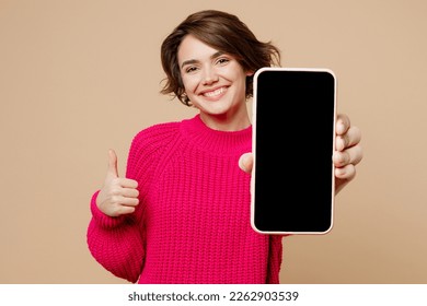 Young happy fun woman wearing pink sweater hold use close up mobile cell phone with blank screen workspace area show thumb up isolated on plain pastel beige background studio. People lifestyle concept - Shutterstock ID 2262903539