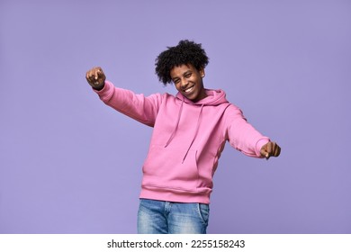 Young happy funky African American teen guy wearing pink hoodie having fun isolated on light purple background. Smiling cool ethnic generation z teenager student model dancing and moving.