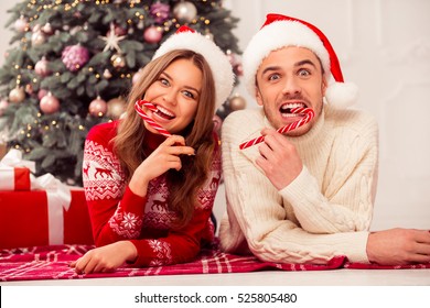 Young happy funny family lying near christmas tree and eating red candy cane