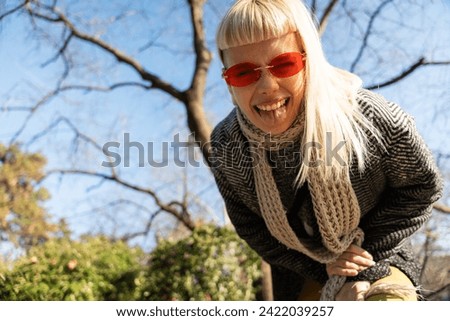 Young happy funny hippie girl showing tongue at camera for fun and making funny faces while wearing cool sunglasses. Attractive female woman enjoying sunny weather expressing her happiness