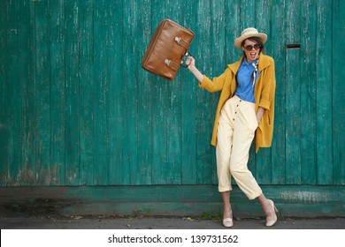 Young happy funny (vintage) dressed woman waves retro suitcase. Old green fence on the background.  Picture ideal for illustating woman magazines. - Powered by Shutterstock