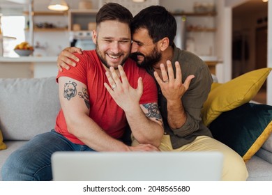 Young happy gay couple in love just got married so they have a video call with their friends and family to spread the joy. The couple showing their wedding rings.