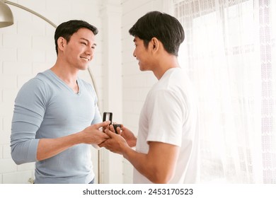 Young happy gay couple in love, proposing and marriage surprise wear a wedding ring in the living room at home. Gay men proposal engagement concept. Surprised partner is very happy. Relationship goal. - Powered by Shutterstock