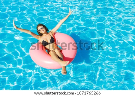 Young happy girl in bikini is swimming in the pool with a pink circle.