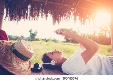 Young Happy Girl Resting Outdoors With Mobile Phone In Hands And Listening Music (intentional Sun Glare And Vintage Color)