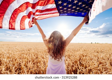 Young happy girl running and jumping carefree with open arms over wheat field. Holding USA flag. Toned image. Selective focus. - Powered by Shutterstock