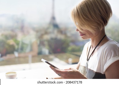 Young Happy Girl With Smile Reading Sms From Smartphone Sitting Near The Panaramic Window In A Cafe In Paris. Eiffel Tower. Sunny Day In Restoran