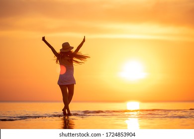 Young happy girl is standing or dancing at sunset beach with raised arms - Powered by Shutterstock