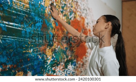 Young happy girl standing and painting colorful stained wall to express idea and enhance imagination with hand print. Caucasian smart girl stamp hand to decorate room in art lesson class. Edification.