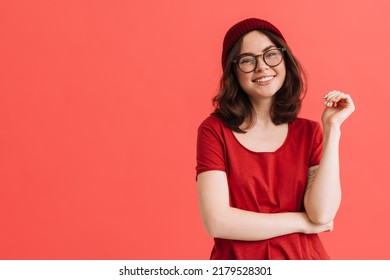 Young happy girl wearing hat and eyeglasses posing at camera isolated over red background - Shutterstock ID 2179528301