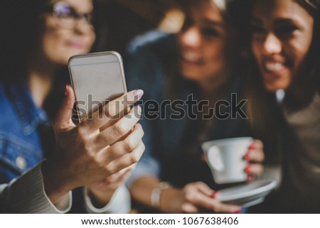 Young happy girls taking self picture in cafe together. Focus on hand.