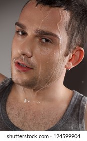 Young and happy guy pouring water on his, studio shot