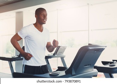 Young happy handsome african-american man in fitness club. Cardio workout, running on treadmill. Healthy lifestyle, guy training in gym. Flare effect, copy space - Powered by Shutterstock