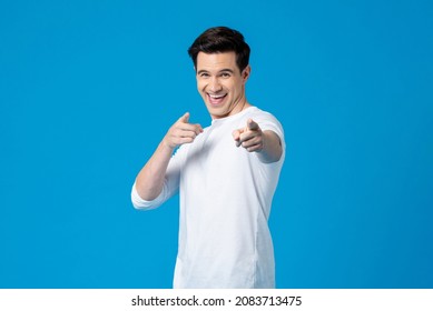 Young happy handsome Caucasian man smiling and pointing fingers at you in isolated light blue background