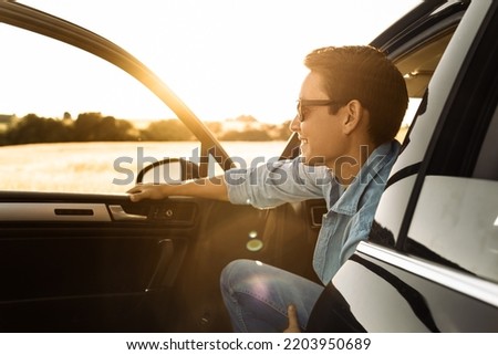 Young happy handsome man sitting in the car smiling watching the sunrise. 