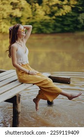 A young happy hippie woman sitting on the lake shore on a bridge in eco clothing made of natural materials in harmony with nature in the fall - Shutterstock ID 2259119409