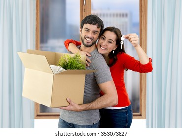 young happy Hispanic couple moving together in a new flat or apartment carrying cardboard boxes home belongings holding house key smiling in housing and real state concept