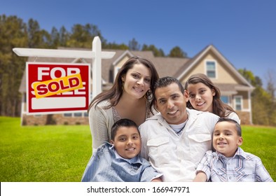 Young Happy Hispanic Young Family in Front of Their New Home and Sold For Sale Real Estate Sign.