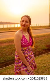 A Young Happy Hispanic Female Standing On A Road Near A Pier During The Sunset