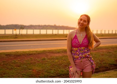 A Young Happy Hispanic Female Standing On A Road Near A Pier During The Sunset