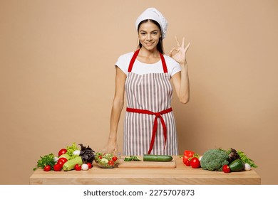 Young happy housewife housekeeper chef cook latin woman wear apron toque chefs hat work at table kitchenware point index finger up isolated on plain pastel light beige background. Process cooking food - Powered by Shutterstock