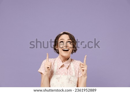 Young happy housewife housekeeper chef cook baker woman wear pink apron point index finger overhead on workspace area mock up isolated on pastel violet background studio portrait. Cooking food concept