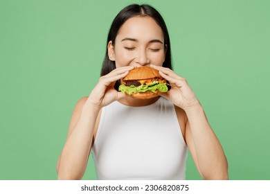 Young happy hungry fun cheerful woman wear white clothes holding eating biting tasty burger isolated on plain pastel light green background. Proper nutrition healthy fast food unhealthy choice concept - Shutterstock ID 2306820875