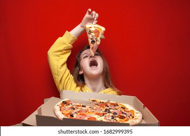 young happy hungry girl eating fresh pizza from a box on a colored background, a student eating fast food with a big appetite