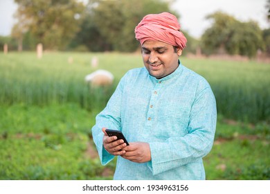 Young Happy Indian Farmer Worker Using Smartphone While Standing In Agriculture Green Field, Internet Banking, 5g Network Technology Concept, Male Wearing Traditional Kurta Outfit.